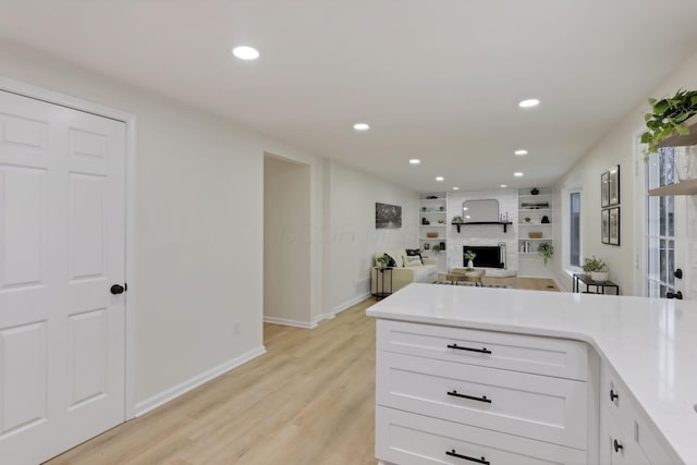 kitchen featuring built in shelves, white cabinetry, a large fireplace, and light hardwood / wood-style floors