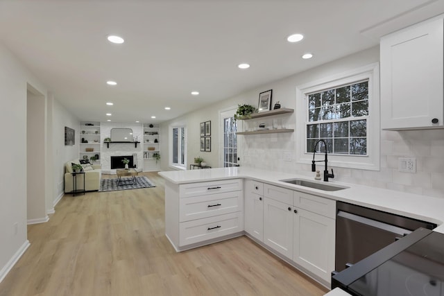 kitchen with decorative backsplash, kitchen peninsula, a fireplace, sink, and white cabinets