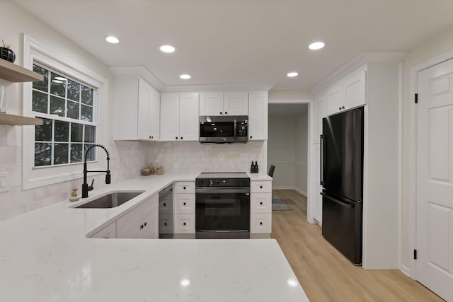 kitchen with decorative backsplash, light wood-type flooring, sink, black appliances, and white cabinetry