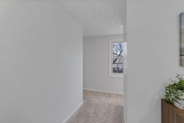 corridor featuring light colored carpet and a textured ceiling