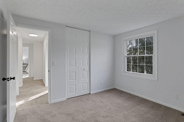 unfurnished bedroom featuring a textured ceiling, light colored carpet, and a closet