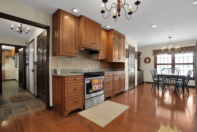 kitchen with an inviting chandelier, decorative backsplash, electric stove, hanging light fixtures, and light stone counters