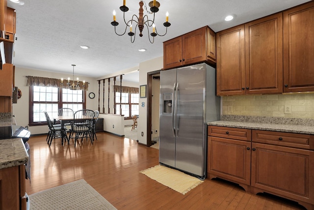 kitchen with tasteful backsplash, light hardwood / wood-style floors, an inviting chandelier, a textured ceiling, and stainless steel fridge