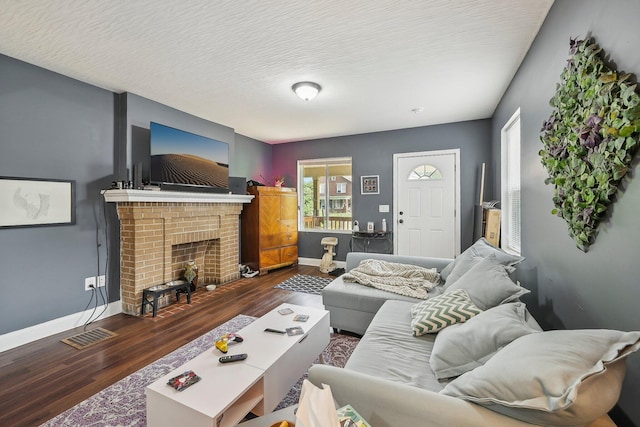 living room featuring a textured ceiling, dark hardwood / wood-style floors, a brick fireplace, and plenty of natural light