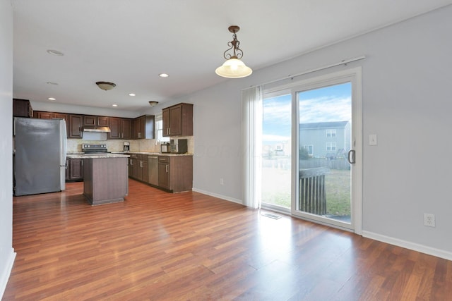 kitchen with stainless steel refrigerator, a center island, hardwood / wood-style floors, and decorative light fixtures