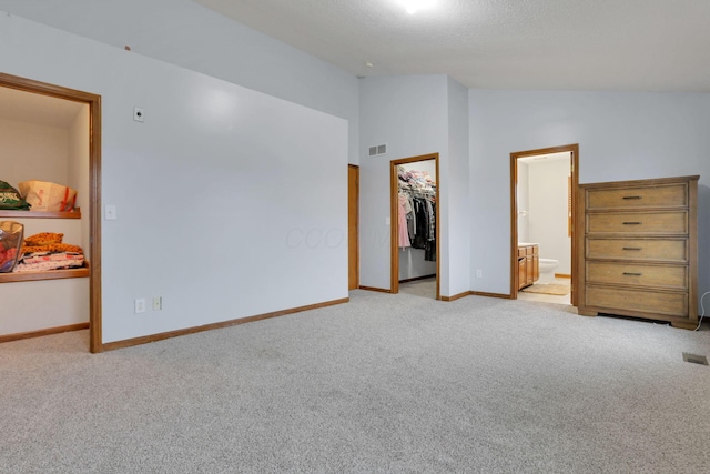 carpeted bedroom with a spacious closet, a closet, ensuite bathroom, and vaulted ceiling