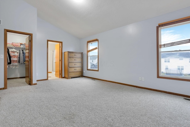 unfurnished bedroom featuring vaulted ceiling, light colored carpet, a spacious closet, and a closet