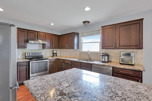 kitchen with dark brown cabinetry, light stone countertops, sink, stainless steel appliances, and decorative backsplash