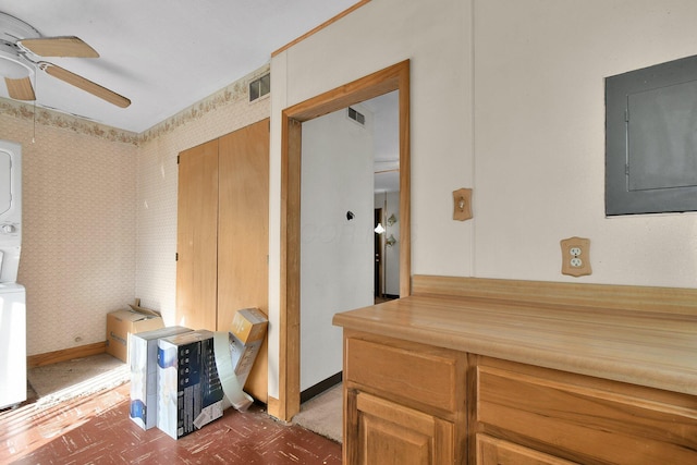 interior space with stacked washer / drying machine, ceiling fan, and electric panel