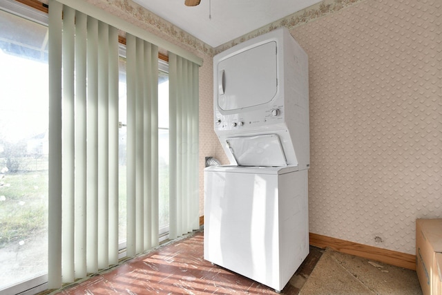 laundry area featuring stacked washer / dryer, ceiling fan, and plenty of natural light