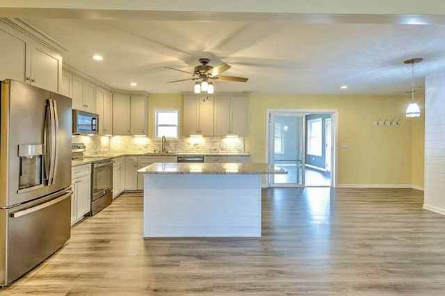 kitchen featuring a center island, sink, light stone countertops, decorative light fixtures, and stainless steel appliances