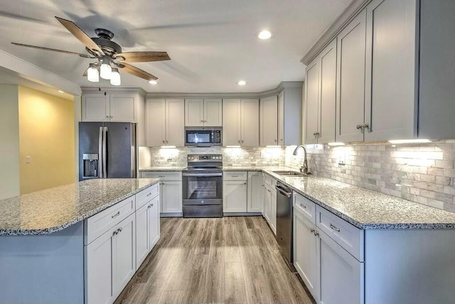 kitchen featuring sink, stainless steel appliances, light stone counters, light hardwood / wood-style flooring, and decorative backsplash