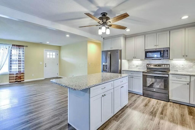 kitchen featuring light stone countertops, appliances with stainless steel finishes, backsplash, light hardwood / wood-style flooring, and a center island