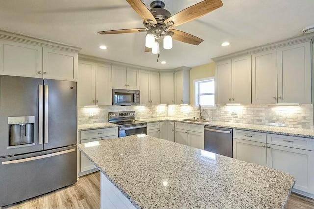 kitchen with appliances with stainless steel finishes, a center island, light stone counters, and sink