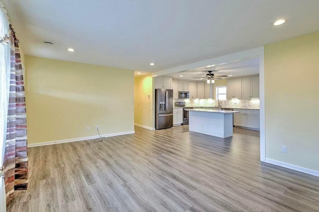 kitchen with decorative backsplash, appliances with stainless steel finishes, ceiling fan, light hardwood / wood-style floors, and a kitchen island