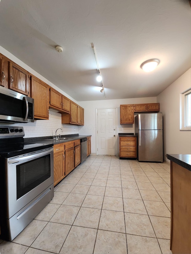 kitchen featuring brown cabinetry, dark countertops, stainless steel appliances, backsplash, and light tile patterned flooring