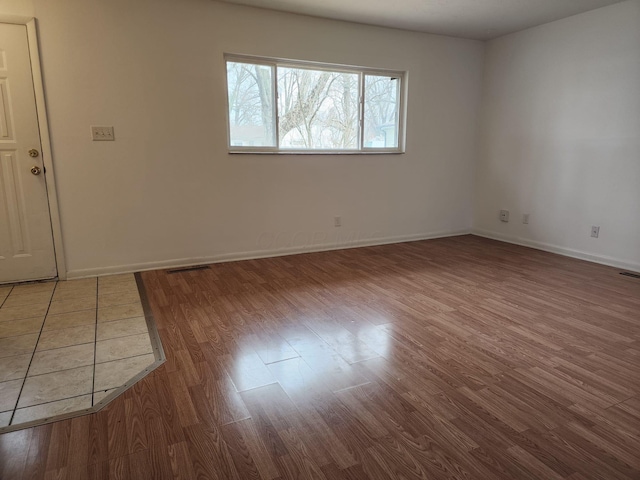 empty room with wood finished floors, visible vents, and baseboards