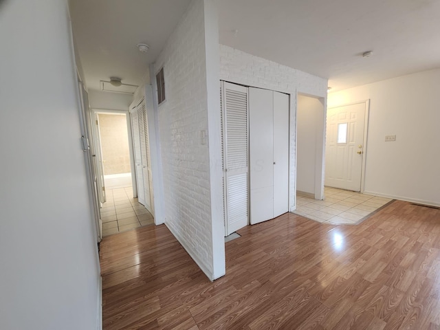 hallway featuring brick wall and light wood-style floors