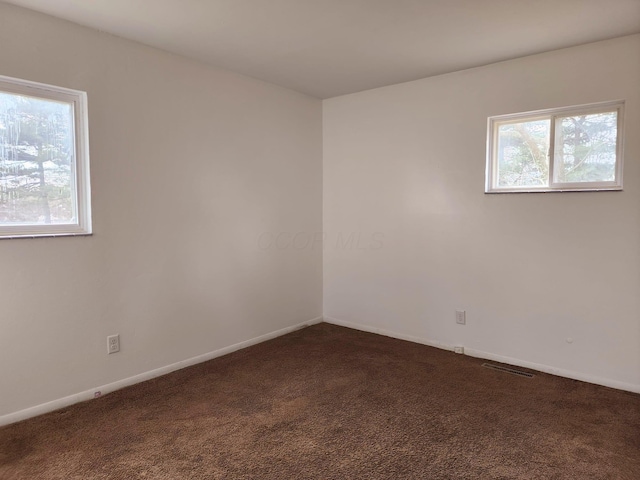 unfurnished room with a wealth of natural light, dark colored carpet, visible vents, and baseboards