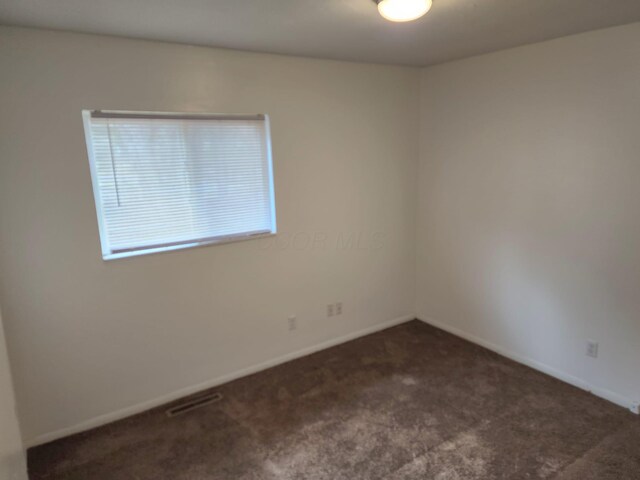 unfurnished room with dark colored carpet, visible vents, and baseboards