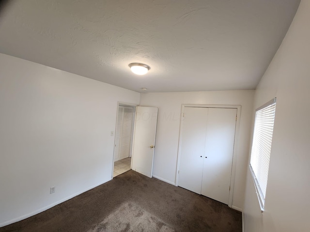 unfurnished bedroom featuring carpet, a closet, a textured ceiling, and baseboards