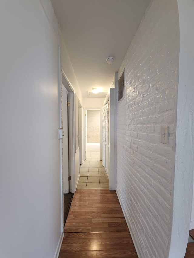 hall featuring light wood finished floors, brick wall, and visible vents