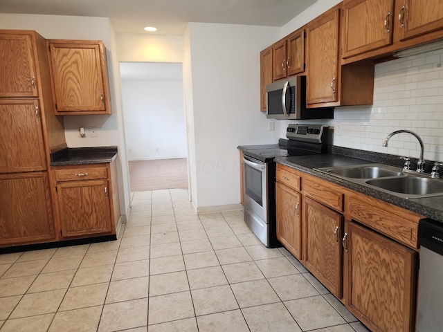 kitchen with appliances with stainless steel finishes, dark countertops, a sink, and tasteful backsplash