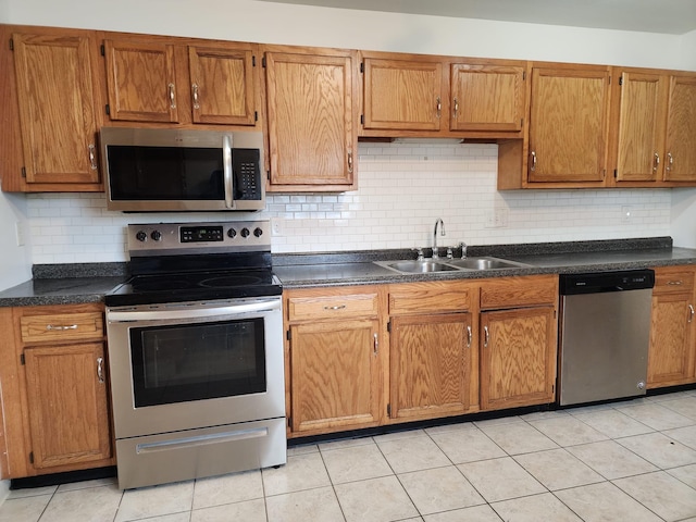 kitchen featuring appliances with stainless steel finishes, dark countertops, a sink, and brown cabinets