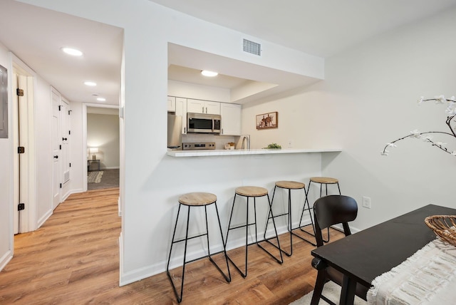 kitchen with kitchen peninsula, appliances with stainless steel finishes, tasteful backsplash, light hardwood / wood-style flooring, and white cabinets