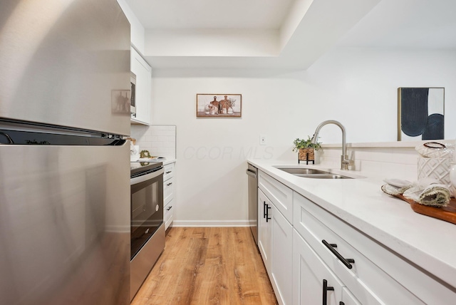 kitchen featuring white cabinets, sink, decorative backsplash, appliances with stainless steel finishes, and light hardwood / wood-style floors