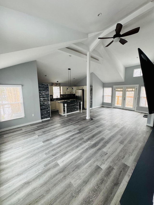 unfurnished living room featuring french doors, ceiling fan, light hardwood / wood-style floors, and vaulted ceiling with beams