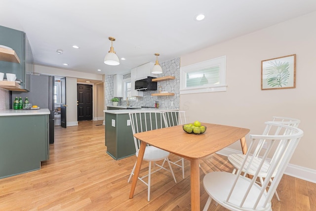 kitchen with light hardwood / wood-style floors, kitchen peninsula, backsplash, and green cabinetry