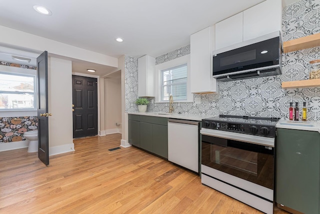 kitchen featuring dishwasher, sink, stove, white cabinets, and light wood-type flooring