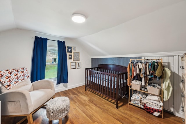 bedroom featuring a nursery area, lofted ceiling, and wood-type flooring