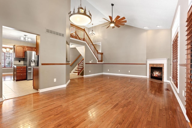 unfurnished living room with ceiling fan, light wood-type flooring, high vaulted ceiling, and a tiled fireplace