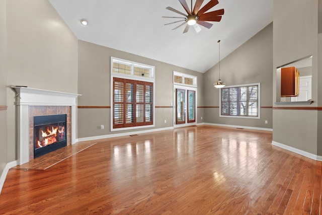 unfurnished living room with hardwood / wood-style floors, ceiling fan, high vaulted ceiling, and a tiled fireplace