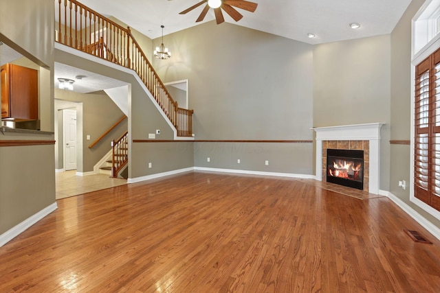 unfurnished living room with a tile fireplace, light hardwood / wood-style flooring, high vaulted ceiling, and ceiling fan with notable chandelier