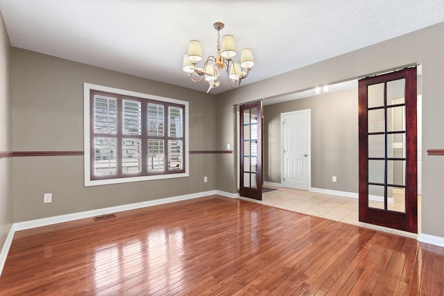 empty room featuring a chandelier, french doors, light wood-type flooring, and a textured ceiling