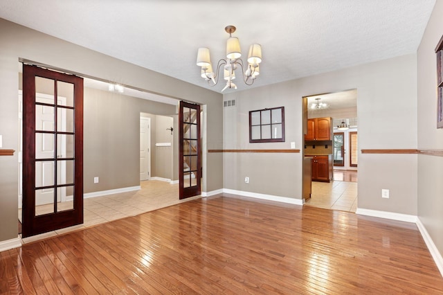 spare room featuring a textured ceiling, a chandelier, light hardwood / wood-style flooring, and french doors