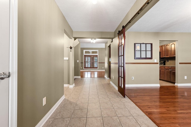 corridor with light tile patterned floors, a barn door, and a textured ceiling