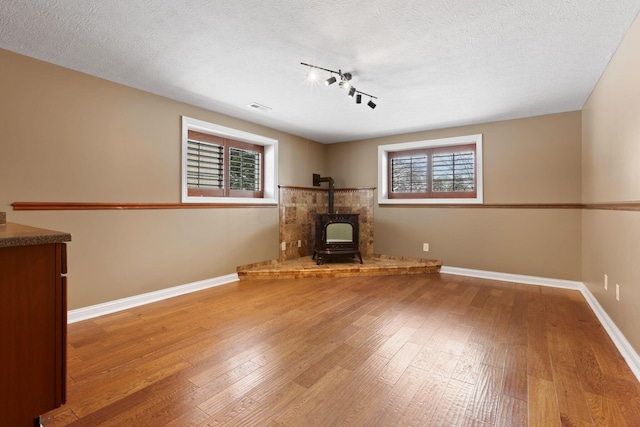 unfurnished living room with wood-type flooring, a textured ceiling, track lighting, and a wood stove