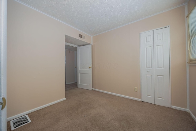 unfurnished bedroom featuring a textured ceiling, light colored carpet, a closet, and ornamental molding