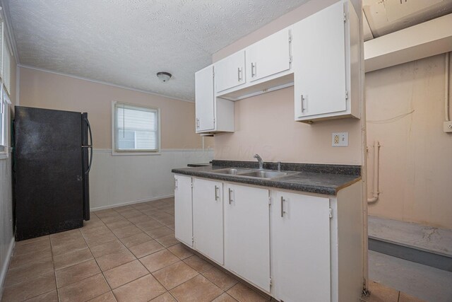 kitchen with black fridge, a textured ceiling, sink, white cabinets, and light tile patterned flooring