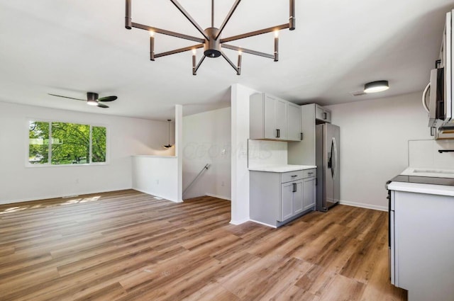 kitchen featuring appliances with stainless steel finishes, gray cabinetry, backsplash, light wood-type flooring, and ceiling fan with notable chandelier