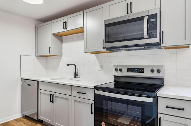 kitchen with appliances with stainless steel finishes, decorative backsplash, light hardwood / wood-style floors, and sink