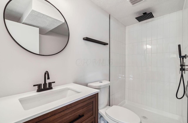 bathroom with toilet, a textured ceiling, tiled shower, and vanity