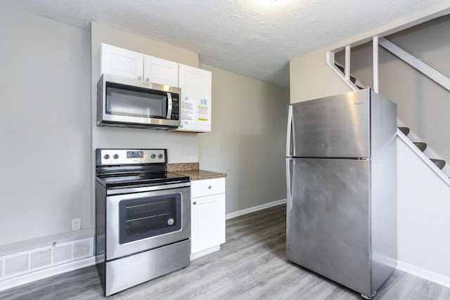 kitchen featuring white cabinets, light hardwood / wood-style floors, a textured ceiling, and appliances with stainless steel finishes