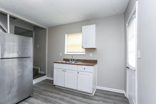 kitchen featuring a textured ceiling, sink, hardwood / wood-style flooring, white cabinets, and stainless steel refrigerator