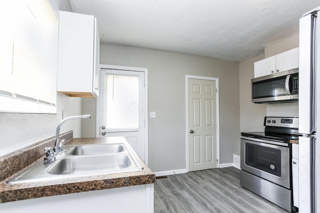 kitchen featuring white cabinetry, sink, light hardwood / wood-style floors, a textured ceiling, and appliances with stainless steel finishes