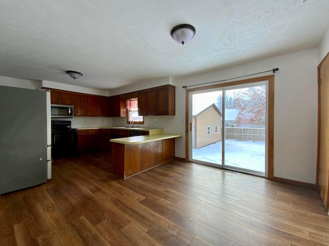 kitchen featuring kitchen peninsula, appliances with stainless steel finishes, dark hardwood / wood-style flooring, a textured ceiling, and sink